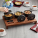 A person putting food into a black Valor mini cast iron pot on a table set with Valor mini cast iron pots filled with food.