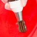 A hand piping chocolate with an Ateco closed star tip on a red surface.