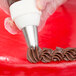 A person using an Ateco closed star piping tip to decorate a cake with chocolate frosting.