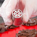 A person holding a metal Ateco 246 Russian piping tip over chocolate.
