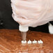 A person using an Ateco Cross-Top piping tip on a pastry bag to decorate a cake.