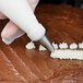 A person's hand using an Ateco cross-top piping tip to decorate a cake with frosting.