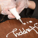 A person using an Ateco oval piping tip to write on a cake with a pastry bag.
