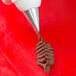 A person using an Ateco pastry bag with a rose leaf tip to pipe chocolate.