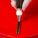 A hand using an Ateco drop flower piping tip to pipe chocolate icing onto a pastry bag.