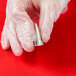 A hand in a plastic glove holding a silver Ateco closed star piping tip.