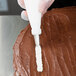 A person using an Ateco leaf piping tip in a pastry bag to frost a chocolate cake.