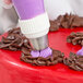 A person using an Ateco pastry bag with a Russian piping tip to decorate a cake with purple frosting.