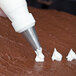 A person using an Ateco drop flower piping tip to pipe white frosting on a brown surface.