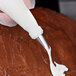 A person using an Ateco leaf piping tip to pipe white frosting on a cake.