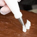 A person using an Ateco open star piping tip and pastry bag to pipe white frosting on a chocolate cake.