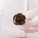 A hand holding a chocolate flower using an Ateco flat stainless steel flower nail.