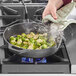 A hand cooking brussels sprouts in a Valor cast iron skillet on a stove.