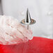 A hand in a glove holding an Ateco stainless steel flower nail with a spike on the top.