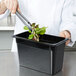 A person using tongs to serve lettuce from a green plant in a black Cambro container.