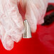 A hand in white gloves using an Ateco Lily-of-the-Valley metal piping tip.
