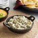 A Valor pre-seasoned mini cast iron casserole dish filled with chips and cheese dip on a table.