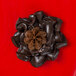 A brown chocolate flower made with an Ateco Russian piping tip on a red surface.