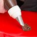 A person using an Ateco leaf piping tip attached to a pastry bag to decorate a cake with chocolate icing.