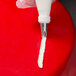 A hand using an Ateco curved petal piping tip to pipe white frosting onto a red surface.