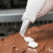 A hand using an Ateco rose piping tip on a pastry bag to frost a chocolate cake.
