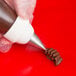 A person using an Ateco rose leaf piping tip to pipe frosting onto chocolate.