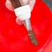 A hand using an Ateco rose leaf piping tip with brown frosting.