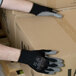 A person wearing Cordova black nylon gloves with gray palm coating holding a box.