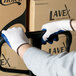 A person wearing Cordova Natural Polyester / Cotton work gloves with blue latex palm coating holding a box.