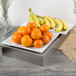 A Tablecraft stainless steel rectangular bowl filled with oranges and bananas on a table in a salad bar.