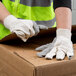 A person wearing Cordova cotton canvas work gloves opening a cardboard box.