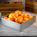 A Tablecraft stainless steel square bowl filled with oranges on a table.