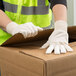 A person wearing Cordova Men's Cotton Reversible Jersey Gloves opening a cardboard box.