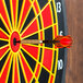 A red and black Arachnid soft tip dart hitting the bullseye of a dartboard.