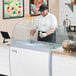 A man wearing a black cap and gloves serving ice cream from a white Avantco Curved Glass Sneeze Guard.