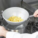 A person using a Vollrath aluminum strainer to drain pasta over a pot.