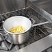 A pot with a Vollrath aluminum strainer of noodles on a stove.