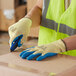 A person wearing Cordova yellow and blue gloves and a safety vest using a cutter to cut a box.