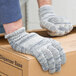 A person wearing Cordova medium weight multi-color jersey work gloves holding a box.