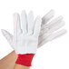 A pair of white gloves with red stitching on the palm.