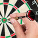 A person holding a Unicorn steel tip dart in front of a dart board.