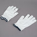 A pair of Cordova medium weight white gloves with a blue band on a gray surface.