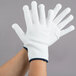 A pair of medium white Cordova nylon work gloves with blue trim on a pair of hands.