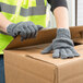 A person wearing Cordova gray work gloves opening a cardboard box.