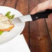A person using a Walco stainless steel steak knife with a black plastic handle to cut meat on a plate.