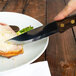 A Walco stainless steel steak knife cutting a piece of meat on a plate.