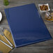 A dark blue Menu Solutions menu board on a table with a fork and knife.