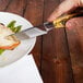 A hand using a Walco steak knife to cut food on a plate.
