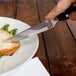 A person using a Walco steak knife to cut meat on a plate with asparagus.