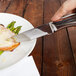 A hand holding a Walco steak knife cutting food on a plate.